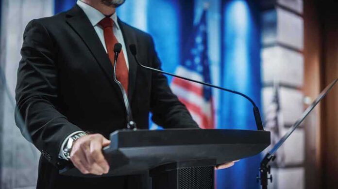 man in suit at podium with microphones