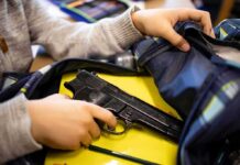 hand reaches into backpack with a handgun inside