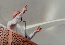 Universities Quietly Rewired Faith Lines – After 9/11 Speaker in traditional attire gesturing from a carved wooden podium