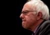 Bernie Sanders in profile wearing glasses against a black background