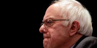 Bernie Sanders in profile wearing glasses against a black background