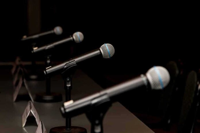 shutterstock_1032429235 Row of microphones on stands at a panel table
