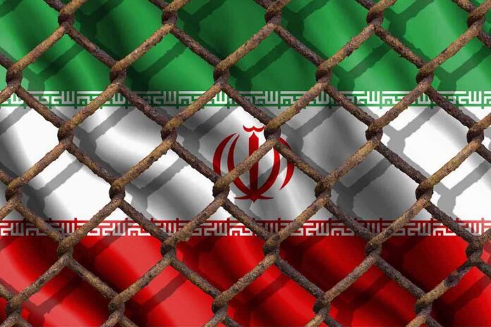 shutterstock_1134760508 Iran flag behind a rusty chain-link fence