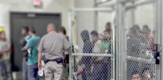 People standing inside chain-link holding area with an officer nearby