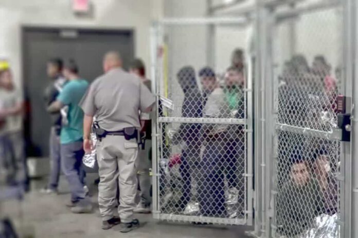People standing inside chain-link holding area with an officer nearby