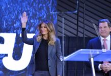 Melania Trump waves on stage beside Eric Bolling at an event