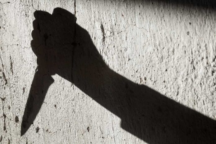 shutterstock_1417367297 Shadow of a hand holding a knife on a textured wall