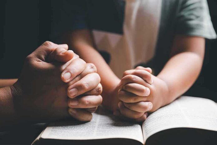Adult and child hands clasped in prayer over an open book