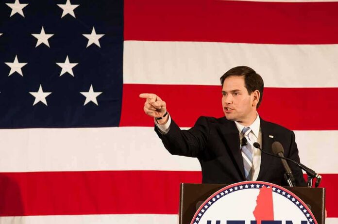 Speaker in suit pointing during speech before large American flag
