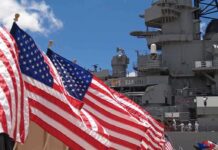 American flags in front of a naval ship under a blue sky